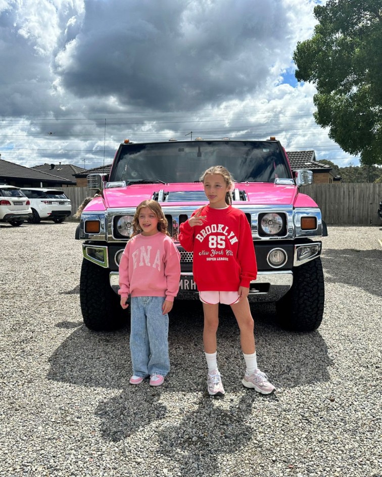 2 girls posing in front of a pink hummer limo
